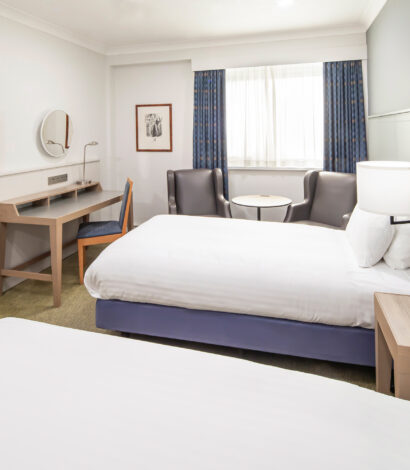 Twin Bedroom decorated crisp white and periwinkle blue. Also in the room 2 wing backed chairs in charcoal grey, dressing table with modern table lamp, side table with telephone and bedside lamps, wall mirror, wall pictures and flat screen TC