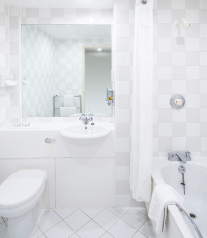 Crisp White Bathroom with Bath, WC and sink with storage. Large Mirror, silver accessories and bath hand rails.