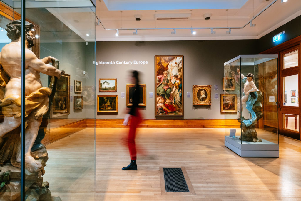 Ferens Art Gallery - © Neil Holmes. 
A gallery inside Ferens Art Gallery, Hull, featuring elegantly displayed paintings in ornate frames. The room is softly lit, with classic and contemporary artworks adorning the walls, offering visitors a rich cultural experience.