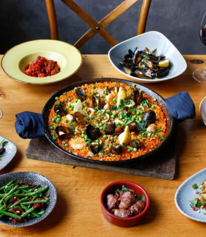 Various Tapas meal options on wooden table with Red wine bottle and wine in glass
