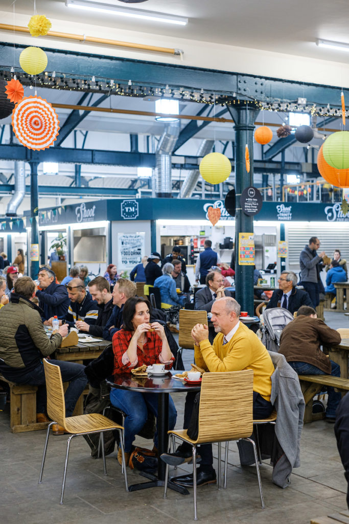 Interior of Trinity Market Food Hall in Hull, a vibrant space with a variety of food stalls and communal seating. The bustling market showcases diverse cuisines, local produce, and a lively atmosphere in a historic setting.