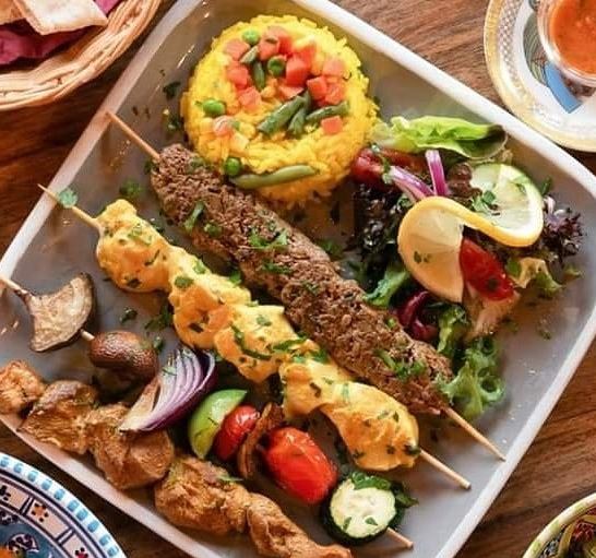 plate of food, brightly colored rice , salad, meat and vegetable kebabs