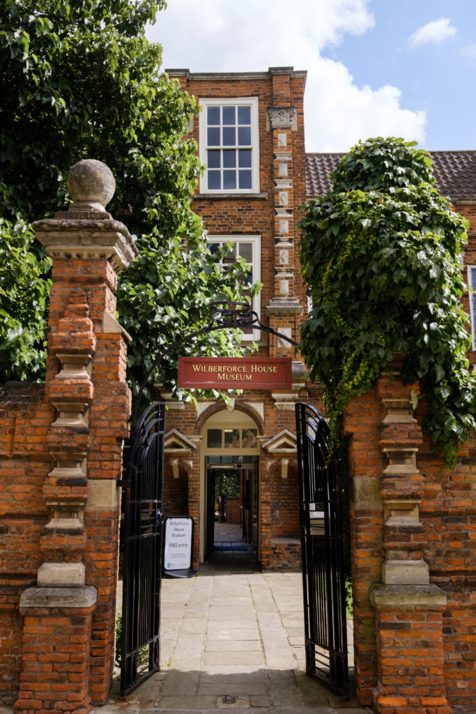 Entrance gate to Wilberforce House, A red brick building built in 1660. Red brick columns and a black wrought iron gate topped with foliage.
