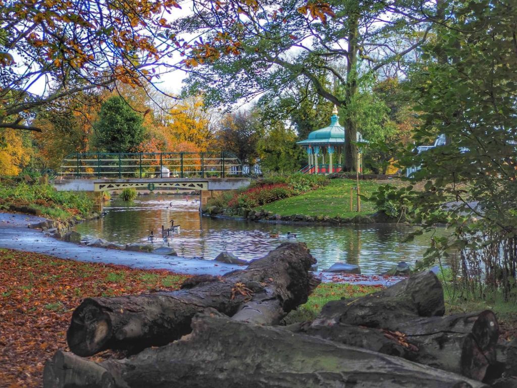 Park pond, surround by trees, a footbridge. Victorian band stand in the background