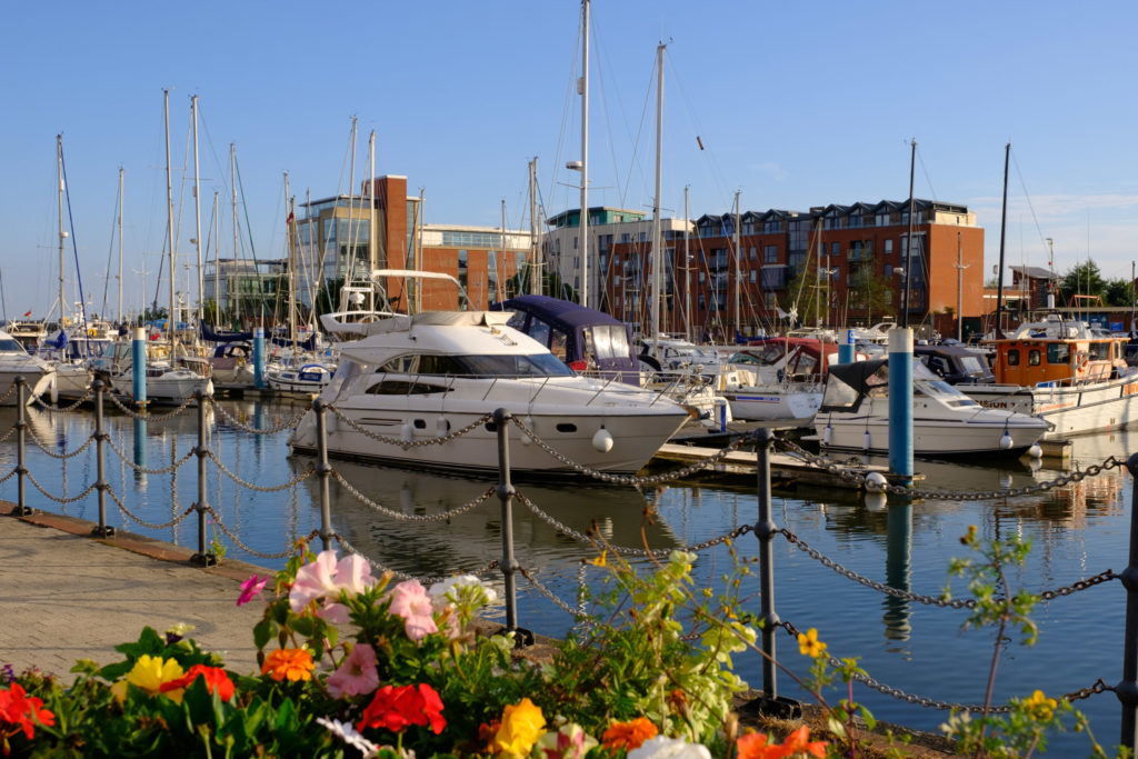 A cruiser moored in Hull Marina, reflecting on the calm waters. The sleek vessel is surrounded by other boats, with the marina’s scenic waterfront and cityscape in the background