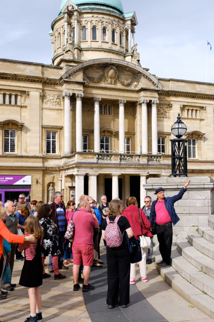 Group if people in front of a white building with column framed entrance and Balcony. 