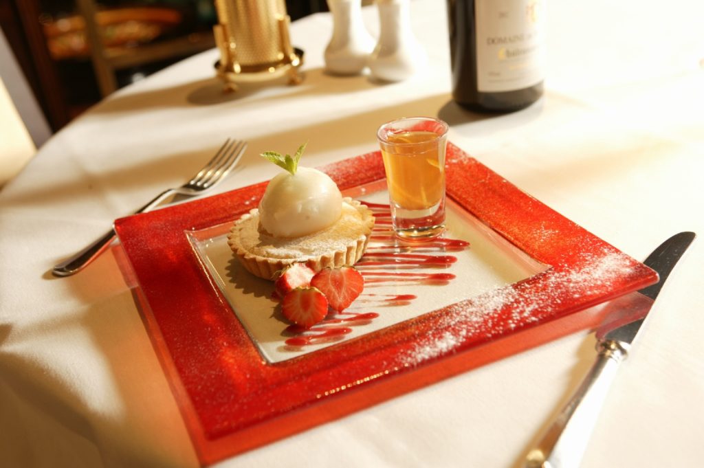 "A plate of ice cream served with a shot glass of glaze at Napoleons Casino. The dessert is elegantly presented, featuring scoops of creamy ice cream and fruit tart alongside a rich, glossy sauce for pouring