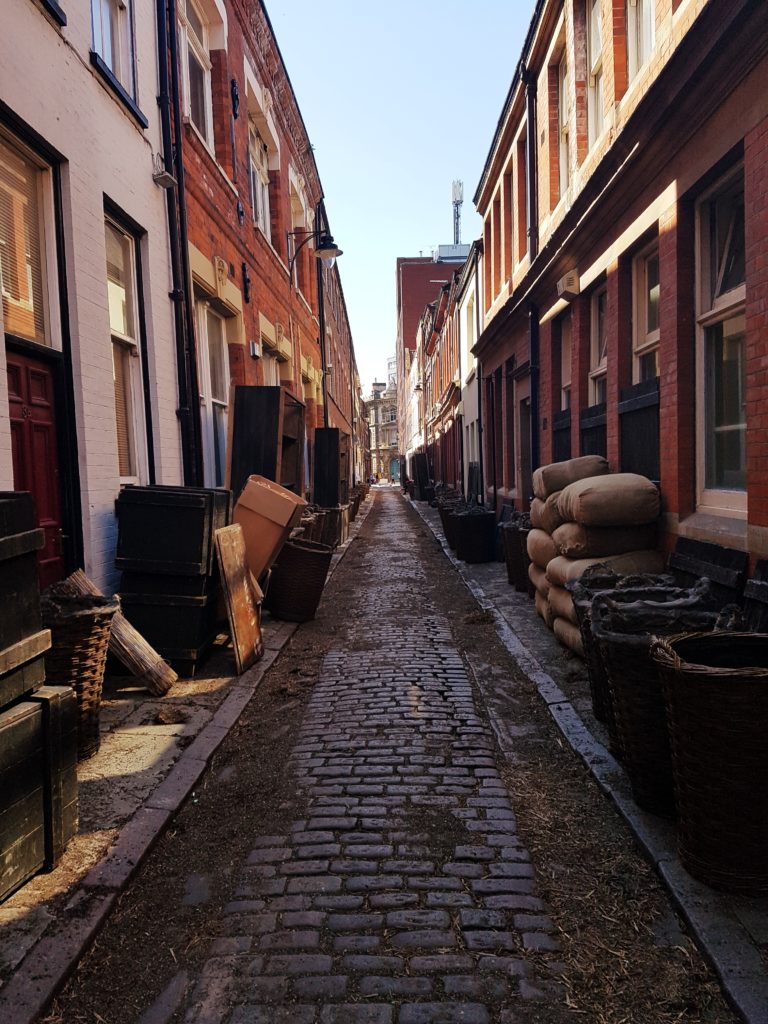 Hulls highstreet, Buildings on either side from various time periods. Cobbles running up the center. The street being is set for a war time movie with the pavements filled with film and sound equipment as well as props including sand bags