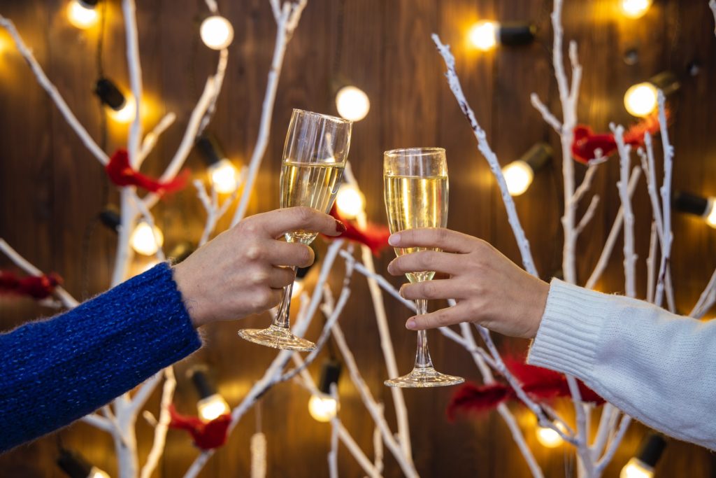 2 arms holding champagne flutes in front of festive white leafless trees and lights 
