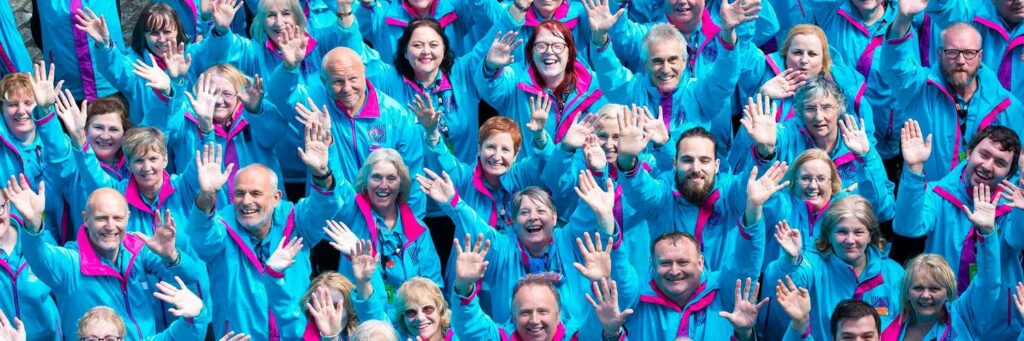 Large group of volunteers on Blue uniforms reaching out looking directly at the camera 