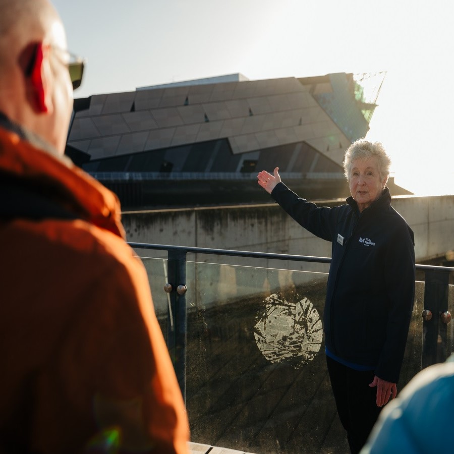 Tour guide standing at the tide defense barrier on the edge of a river pointing towards the Deep