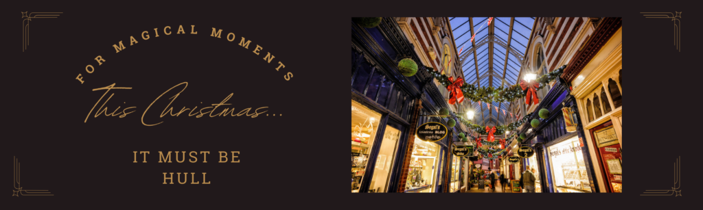 Victorian shopping arcade with glass roof. Shops line either side. from the roof are Christmas garlands of green foliage and red ribbons