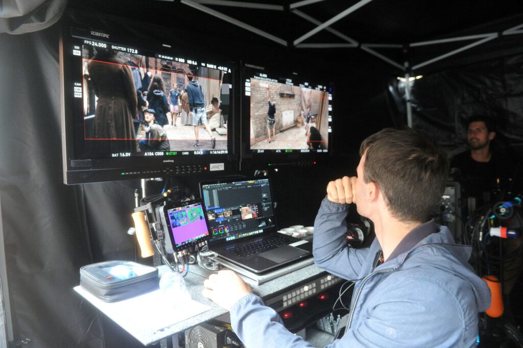 Filming desk with laptop and various screens picturing filming taking place 