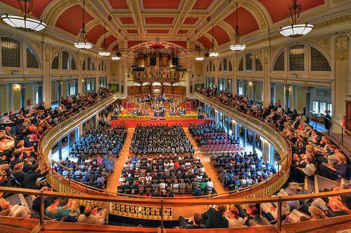 An orchestral performance at Hull City Hall, with musicians seated on a grand stage under warm lighting. The historic venue’s elegant architecture and high ceilings provide a stunning backdrop for the live classical music event
