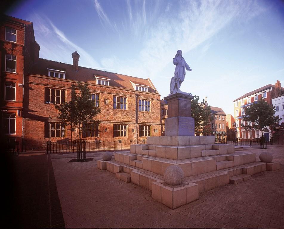 Trinity Square in Hull, featuring the Hands on History Museum, formerly the Old Grammar School, housed in a historic brick building. In the foreground stands a statue of Andrew Marvell, the 17th-century poet and politician, commemorating his legacy."
