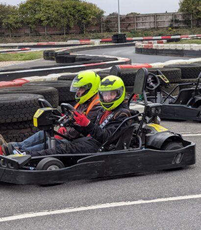 2 people in full face helmets in a go kart on a race track