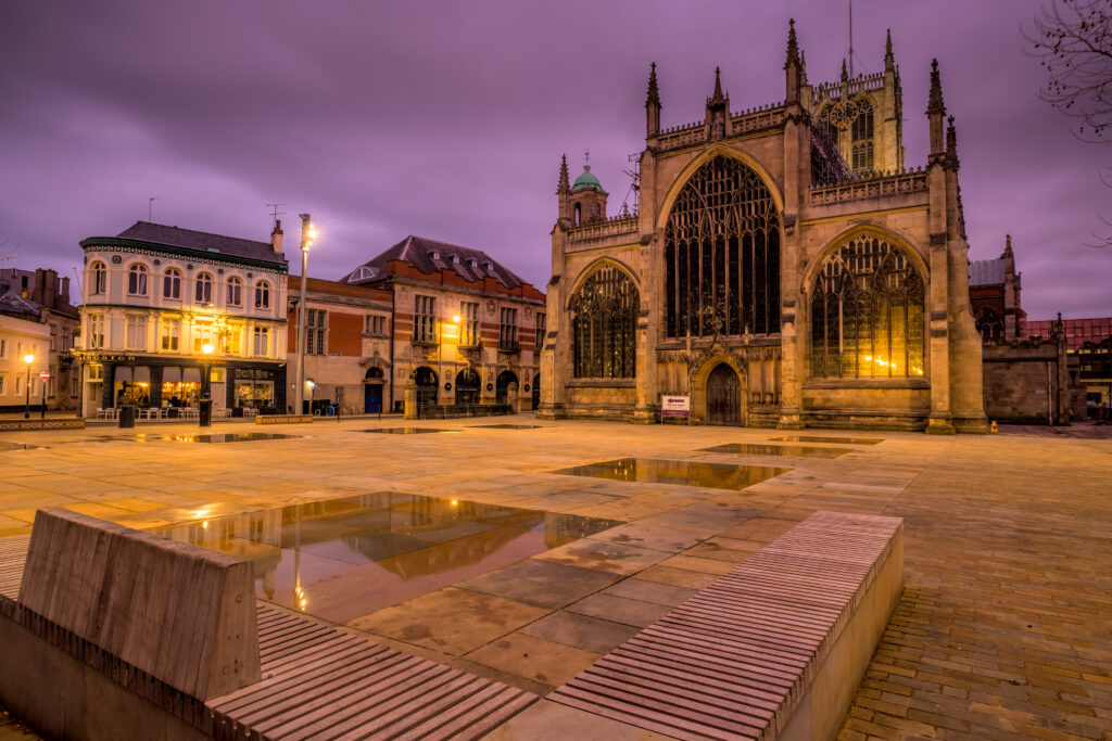 Hull Minster Large Gothic Church set in Market square surrounded by historic buildings and mirror pools reflective the church. All set against purple sky