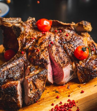 Large Medium cooked steak with fried tomatoes on butcher block board