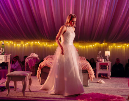 Baby He Loves You, woman in a white wedding dress surrounded by pink lighting.